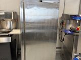 un réfrigérateur en acier inoxydable dans une cuisine, avec d'autres appareils électroménagers en arrière-plan