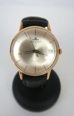 une montre en or posée sur un socle noir, sur une surface blanche
