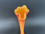 orange and yellow vase with a flower shaped stem on a black surface