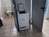 a small refrigerator in the middle of a bathroom with a toilet in the background