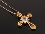 a gold cross pendant with a clear stone on a black surface