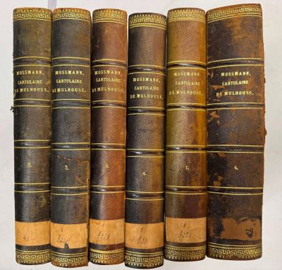 six vieux livres sont alignés sur une surface blanche