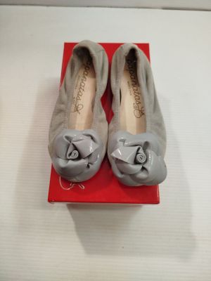une paire de chaussures grises ornées de nœuds sur le bout, présentée dans une boîte rouge