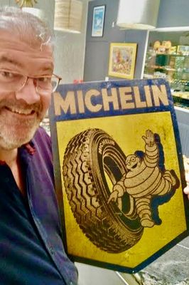 un homme souriant tenant une pancarte « Michel Tire » dans un magasin