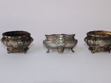 trois vases en argent posés l'un à côté de l'autre sur une surface blanche
