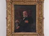 portrait of a man in a black suit and a white beard in a gold frame