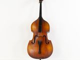 un vieux violoncelle posé sur un pupitre, adossé à un mur blanc