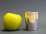 a yellow apple next to a silver cup on a table