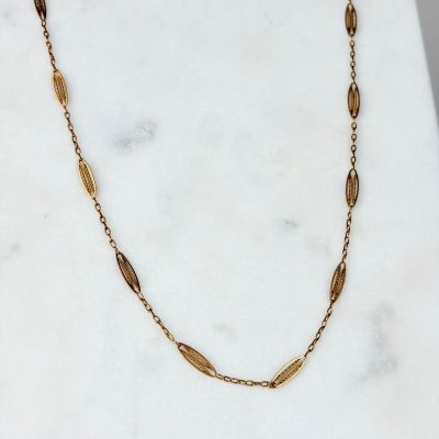 un gros plan d'un collier en or posé sur une surface en marbre
