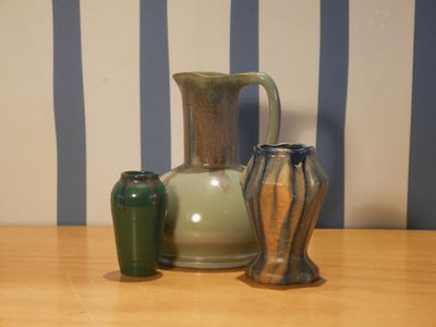 trois vases posés sur une table, avec un mur rayé en arrière-plan
