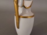 a white and gold vase with a curved handle