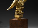 an image of a golden statue of an eagle on a wooden pedestal