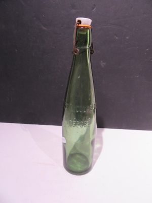 a green glass bottle with a gold cap sitting on a white table