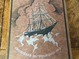 an old book on a wooden table with a picture of a ship in the background
