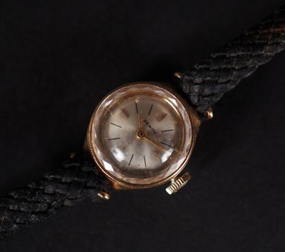 an old gold watch with a black leather strap on a black surface