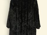 black faux fur coat on a hanger against a white wall