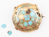 turquoise and gold broochle on a white surface with broken glass