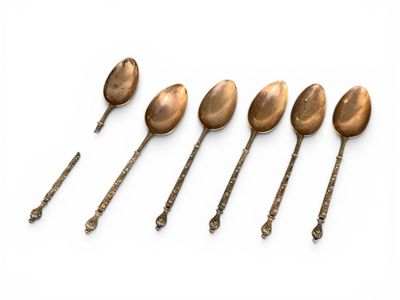 six antique spoons are lined up in a row on a white surface