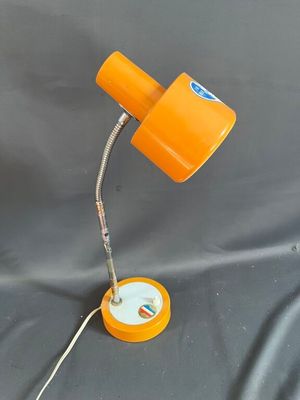 une lampe de bureau orange, avec son cordon, posée sur une surface grise