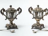two silver vases with spoons and spoons on them