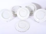five white plates on a white table with a red vase
