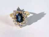 une photo d'une bague sertie d'un saphir bleu et de diamants, posée sur une surface blanche