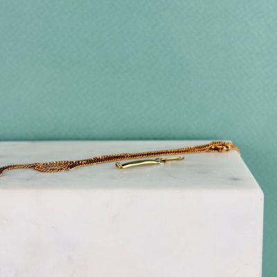 un gros plan d'un collier en or posé sur un bloc de marbre blanc