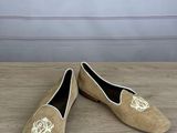 pair of beige sued shoes with a gold monogram on the heel
