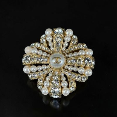 a close up of a pearl and gold broochle on a black surface