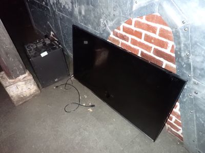 un téléviseur noir posé par terre près d'un mur de briques