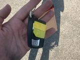 une main tenant une clé de voiture sur laquelle est collé un autocollant jaune