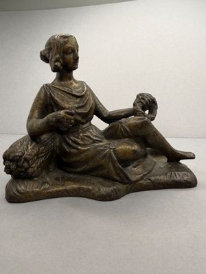 statue en bronze représentant une femme assise sur un rocher avec un chien