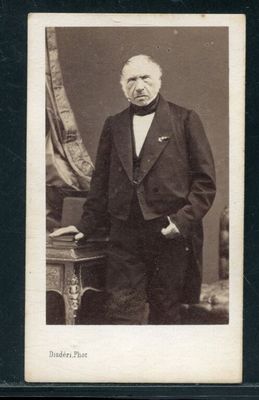 portrait d'un homme en costume et nœud papillon, debout devant une table