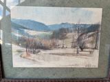 painting of a landscape in a frame on a table with a window in the background