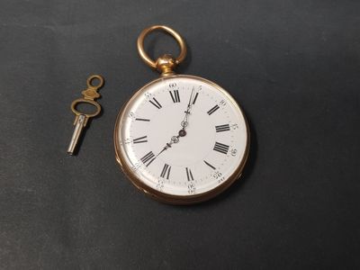 une montre de poche en or et une clé posées sur une table