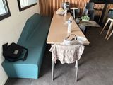 une longue table sur laquelle est posé un sac, à côté d'un banc bleu