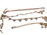 three gold necklaces and a pair of earrings on a white surface
