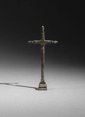 an image of a bronze cross on a pedestal with a shadow on the ground