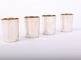 quatre tasses en argent sont alignées les unes à côté des autres sur une surface blanche