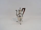 une cafetière ancienne en argent, posée sur un support et dotée d'une poignée en bois