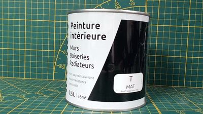 un pot de peinture posé sur un tapis de découpe, à côté d'une règle