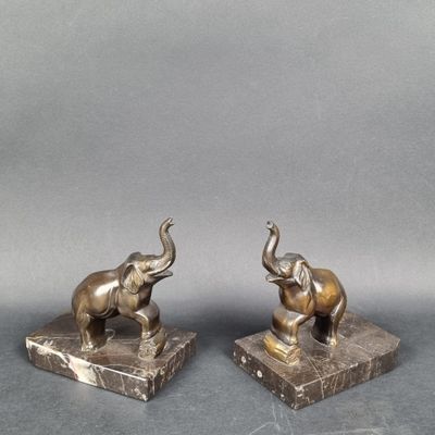 pair of bronze elephants on marble bases on a gray background