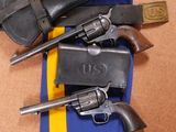 deux revolvers et un étui fixés à une ceinture rayée bleue et jaune