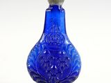 une vieille bouteille en verre bleu munie d'un bouchon en métal, posée sur une surface blanche