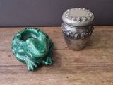 a green frog sitting next to a silver container on a wooden table