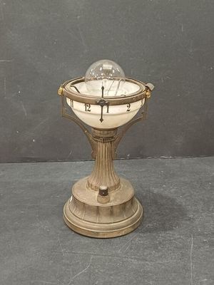 une horloge posée sur un socle, surmontée d'une boule de verre