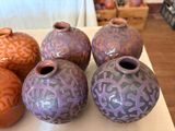 five vases sitting on a table with a basket of apples in the background