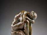 a bronze statue of a man sitting on a rock with his head in his hands