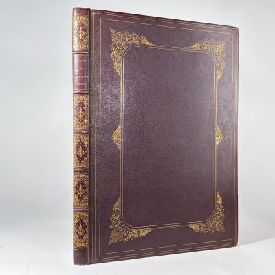 un livre marron aux tranches dorées posé sur une surface blanche