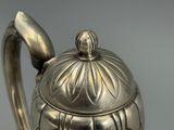 une théière en argent avec son couvercle, posée sur une table